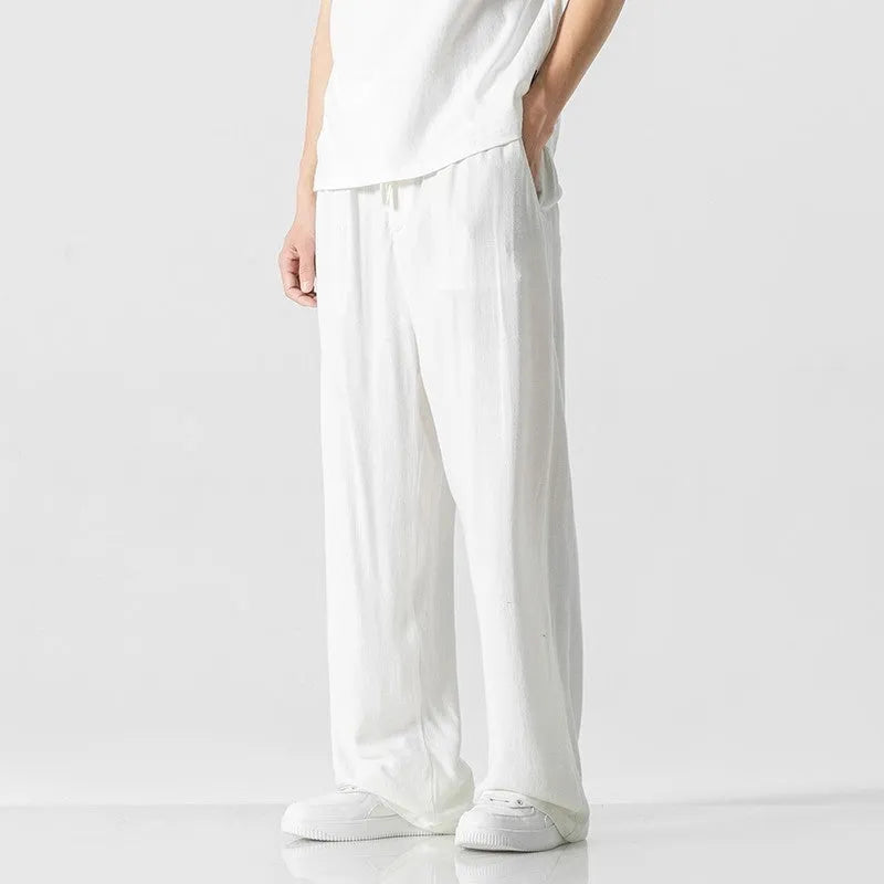 Men's beige linen-style trousers with a loose straight-leg fit and drawstring waist, laid flat.