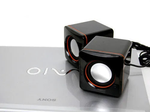Small black square USB-powered computer speaker with audio and USB cables