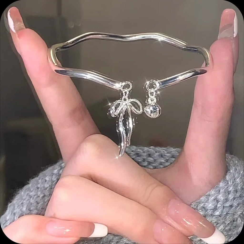 Silver adjustable bracelet with bow and bell charms on wrist showing opening clasp