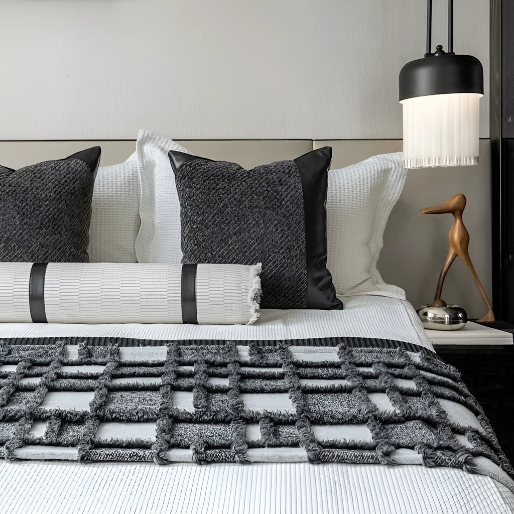 Grey and white plaid bed runner blanket with matching pillowcase and round leather-look pillow on a bed.