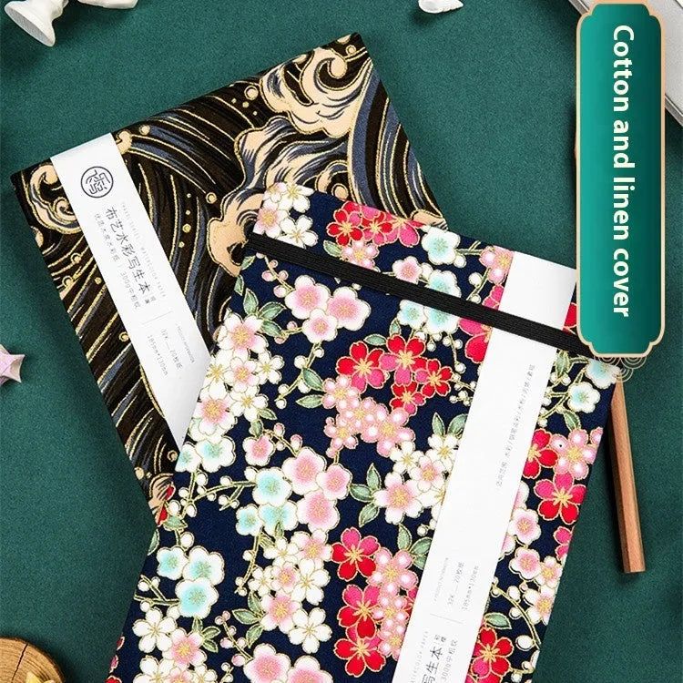 Feiluniao fabric-covered watercolour notebook open on a table with art supplies.