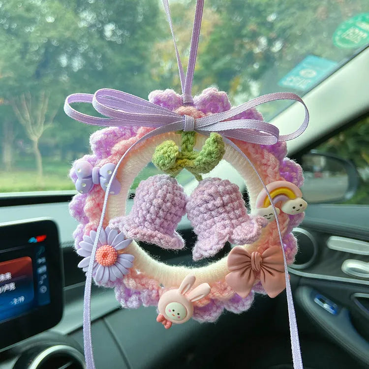 Handwoven wool bell orchid flower car pendant on a green background.
