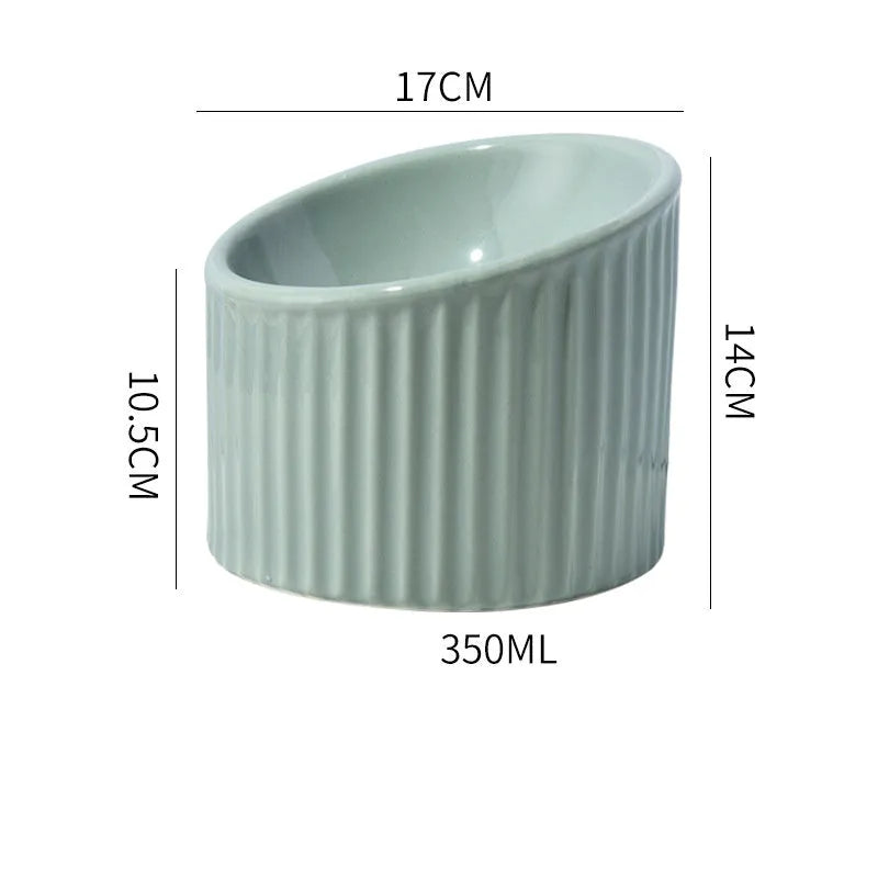 Dark green ceramic elevated cat bowl on a table, showing its raised height and round, tilted shape.