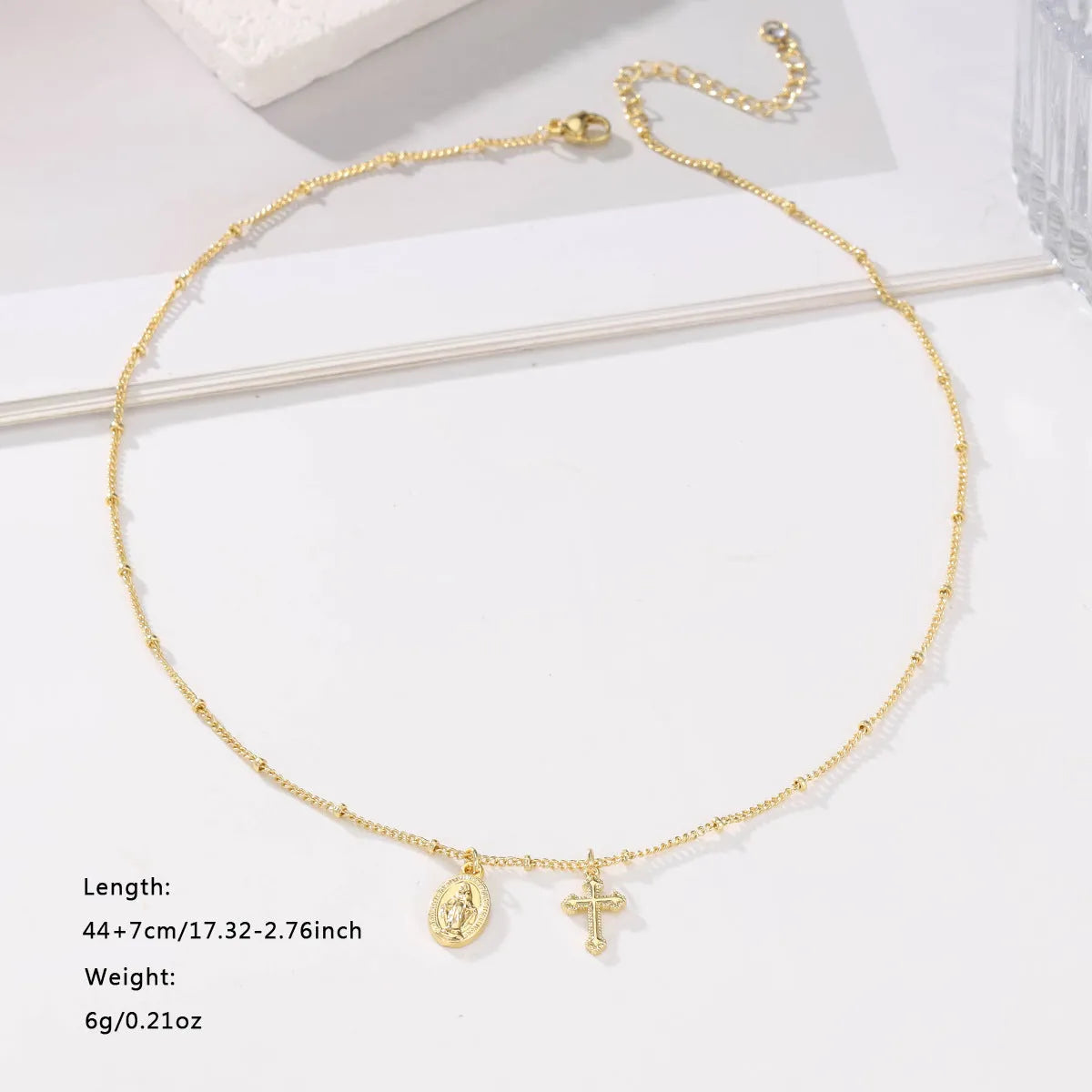 Gold coloured geometric cross Virgin Mary pendant necklace on a chain.