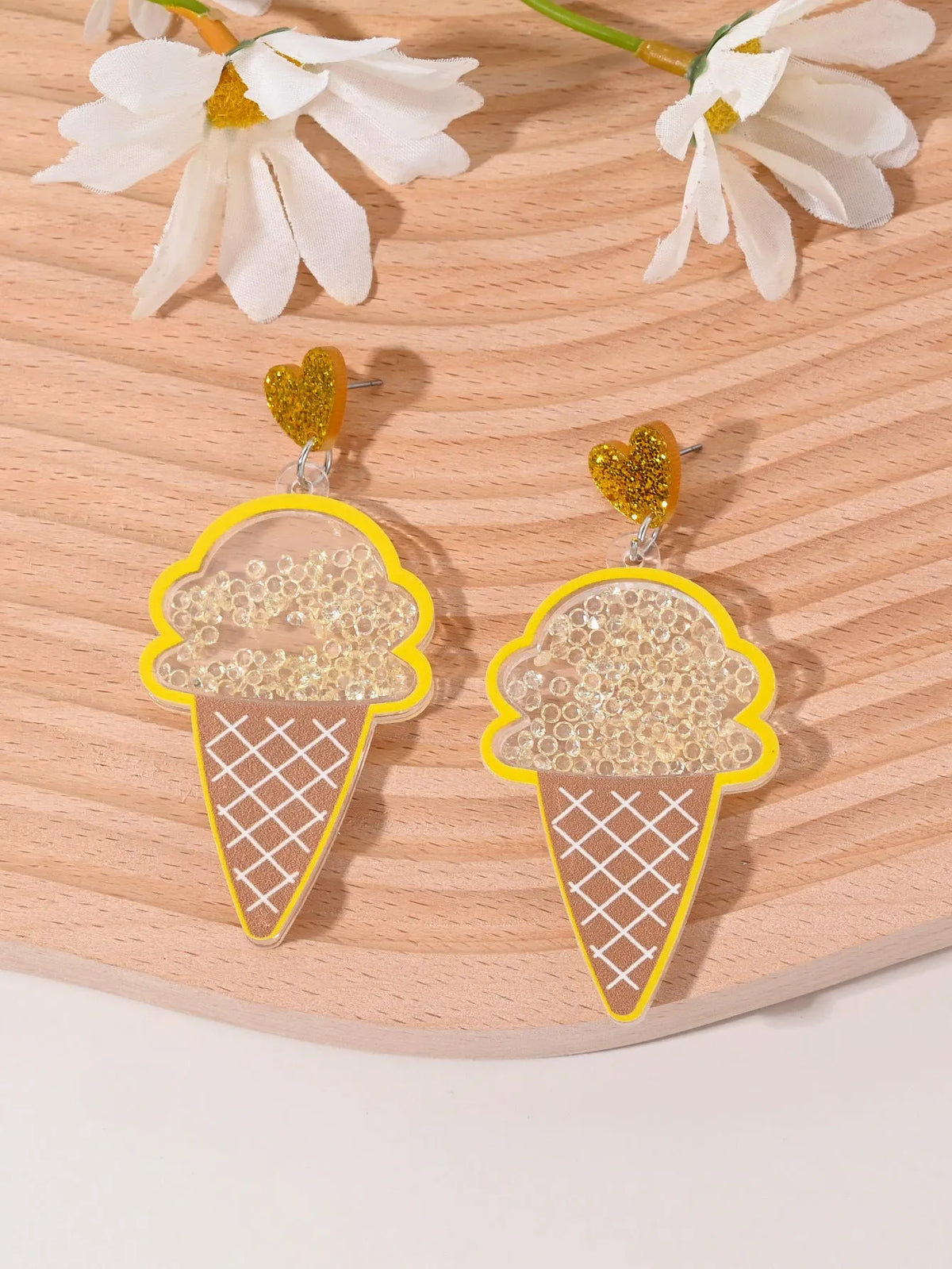 A pair of colourful acrylic earrings with a cake design next to other fruit and ice cream style earrings.