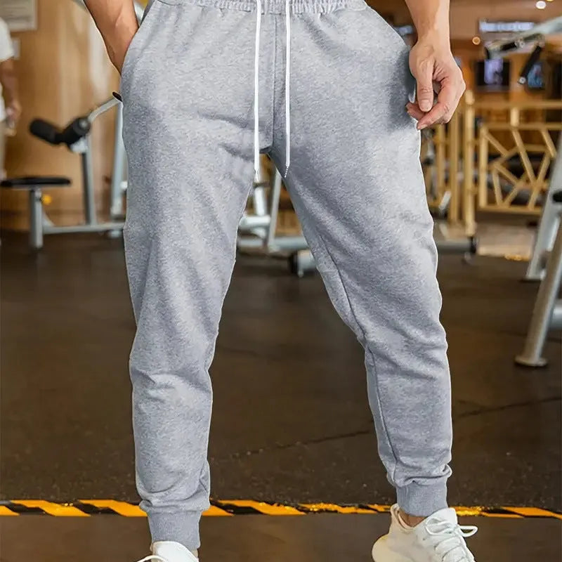 Man wearing loose grey linen-style trousers with an elastic drawstring waist, side view.