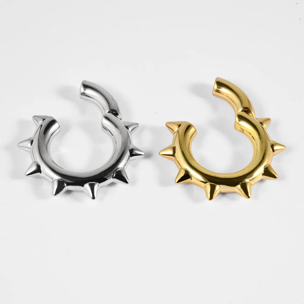 A pair of sharp cone-shaped copper ear extenders with a round magnetic closure on a flat surface.