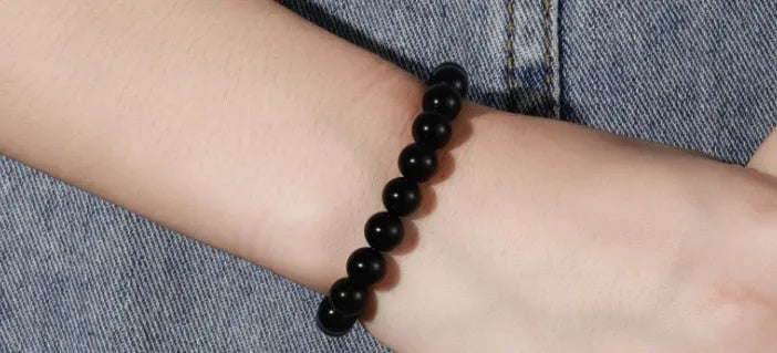 Close-up of a women's black onyx bracelet with 8mm geometric agate beads on a black elastic cord.