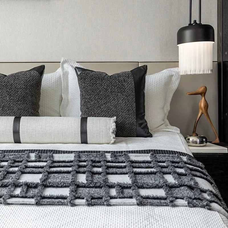 Grey and white plaid bed runner blanket with matching pillowcase and round leather-look pillow on a bed.