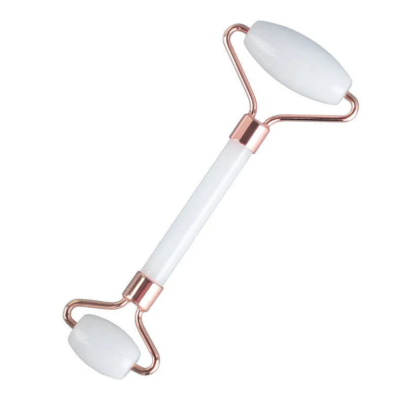 White jade facial roller and gua sha scraper board set on a plain surface.