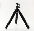 Black flexible octopus tripod with bent legs holding a smartphone on a table.