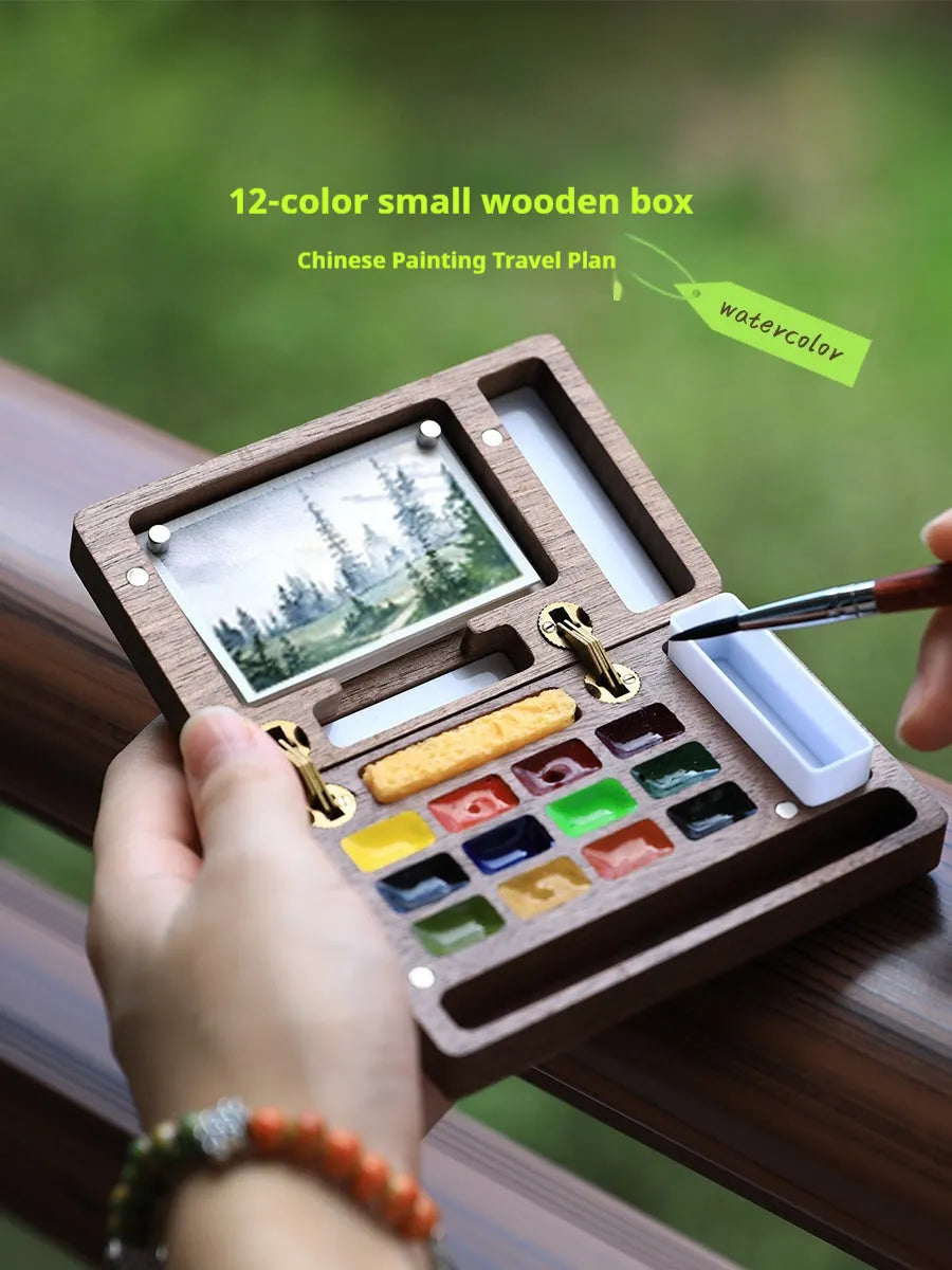 Mini solid walnut wood watercolour paint box with open lid showing internal compartments for half-pan pigments.