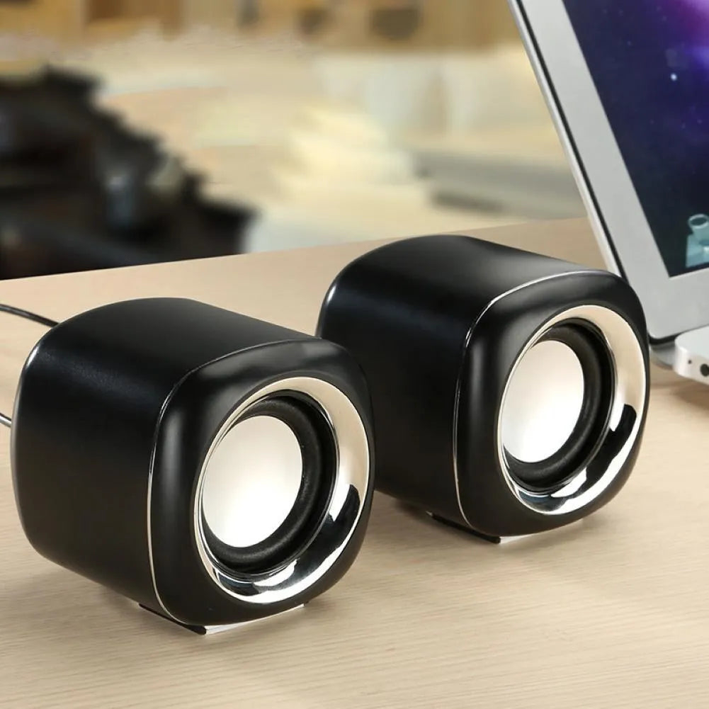 A pair of small black wired computer speakers on a desktop next to a laptop.