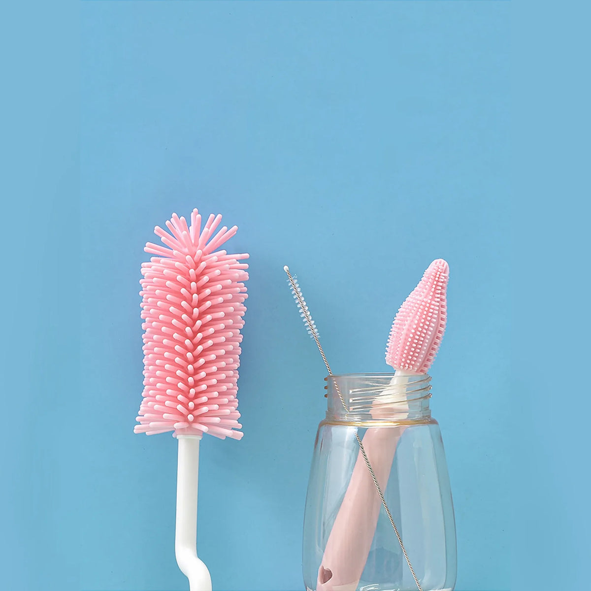 Silicone baby bottle brush with straw cleaning attachment in pink, blue, and yellow colours