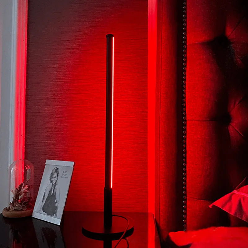 Tall black Nordic minimalist table lamp with RGB LED light on a wooden bedside table.