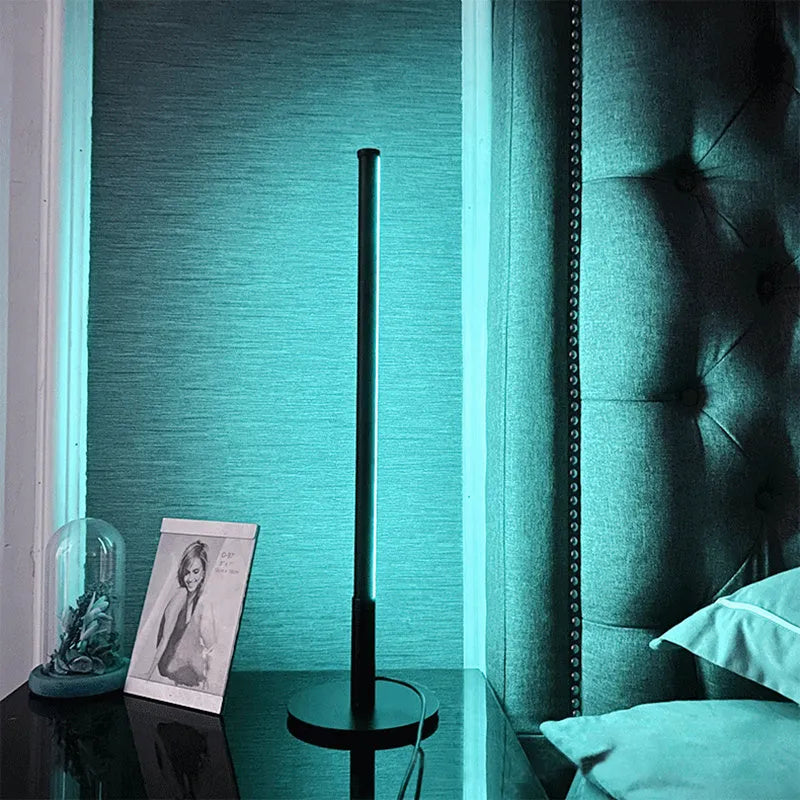Tall black Nordic minimalist table lamp with RGB LED light on a wooden bedside table.