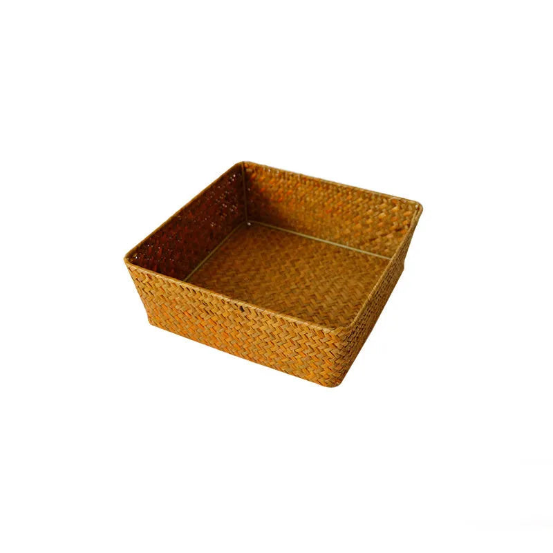 Woven straw desk storage box with lid in brown, shown alongside cosmetics and pens.