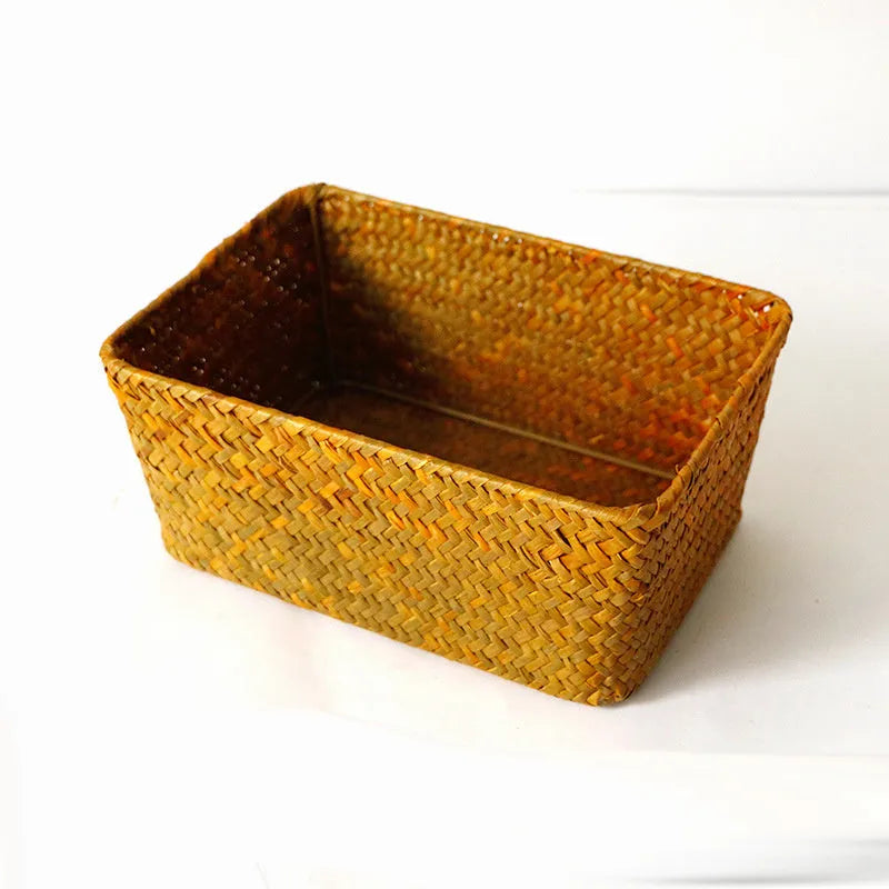 Woven straw desk storage box with lid in brown, shown alongside cosmetics and pens.