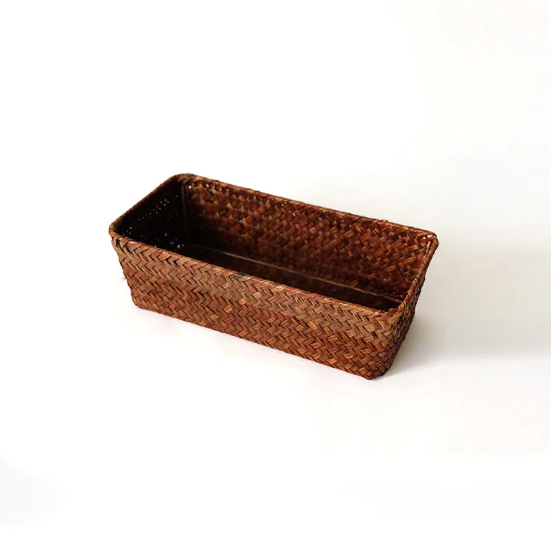Woven straw desk storage box with lid in brown, shown alongside cosmetics and pens.