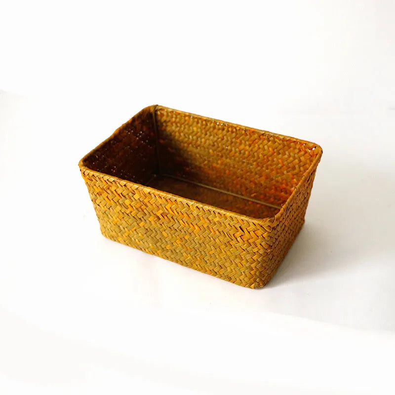 Woven straw desk storage box with lid in brown, shown alongside cosmetics and pens.
