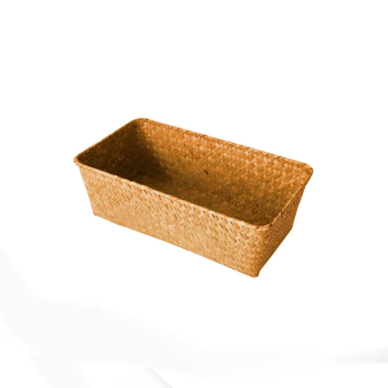 Woven straw desk storage box with lid in brown, shown alongside cosmetics and pens.
