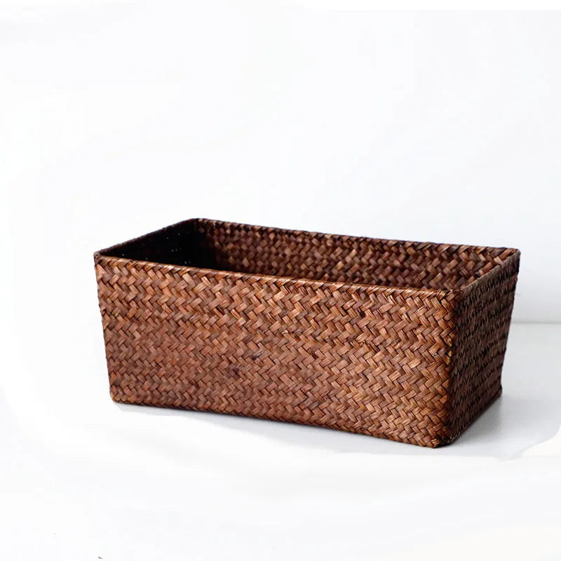 Woven straw desk storage box with lid in brown, shown alongside cosmetics and pens.
