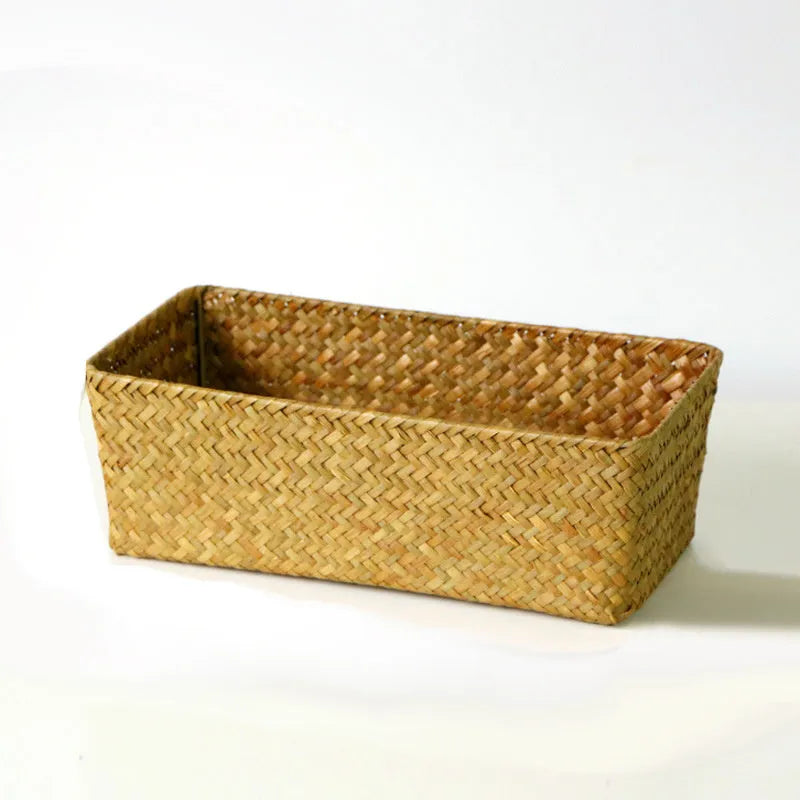 Woven straw desk storage box with lid in brown, shown alongside cosmetics and pens.