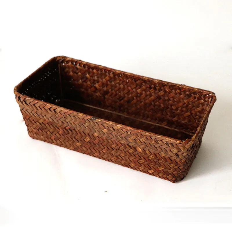 Woven straw desk storage box with lid in brown, shown alongside cosmetics and pens.