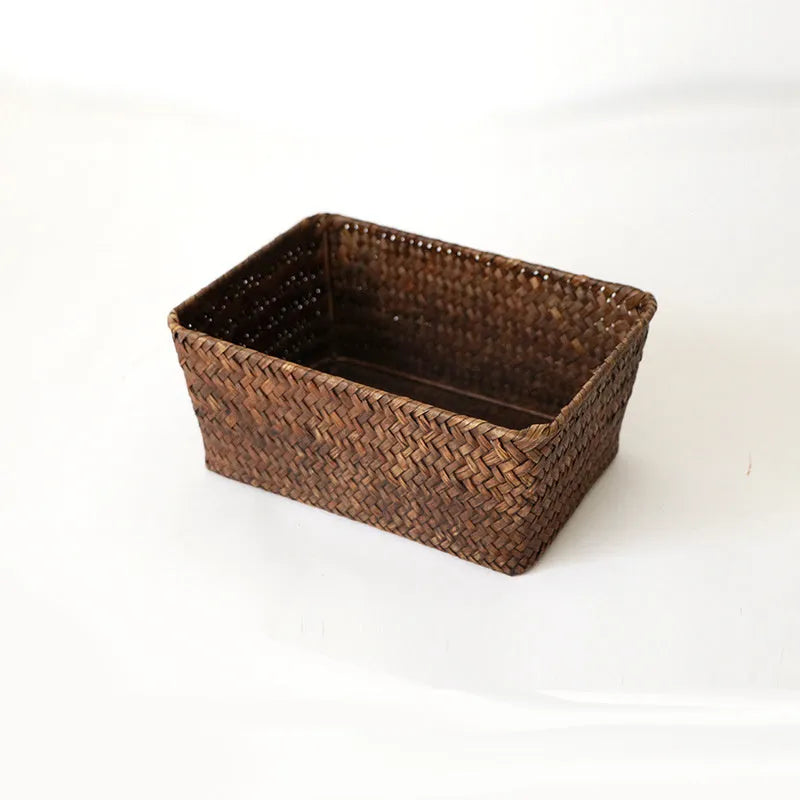 Woven straw desk storage box with lid in brown, shown alongside cosmetics and pens.