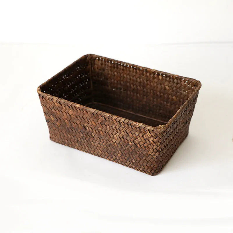 Woven straw desk storage box with lid in brown, shown alongside cosmetics and pens.