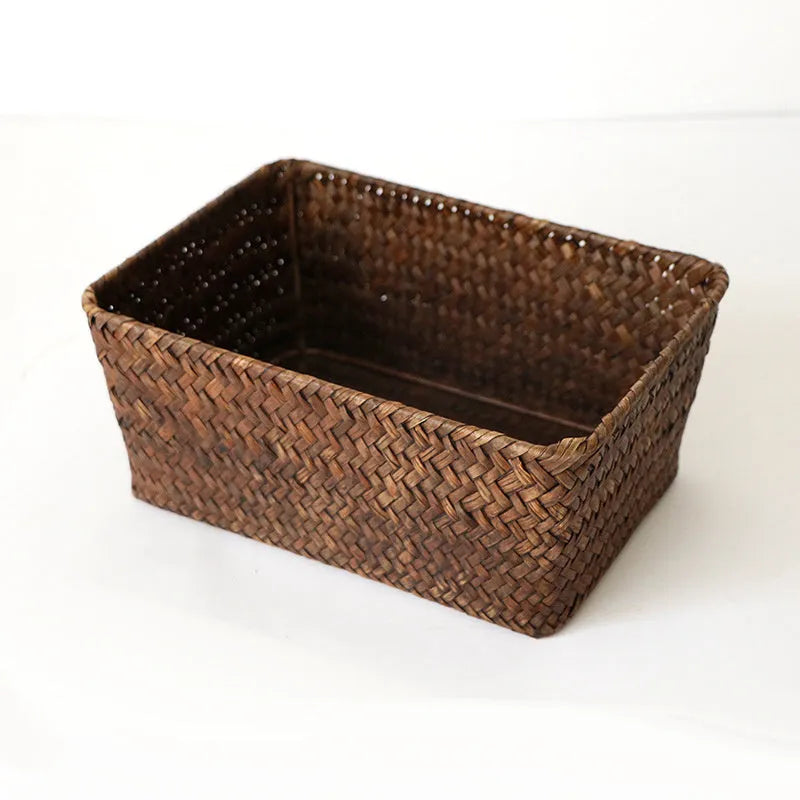 Woven straw desk storage box with lid in brown, shown alongside cosmetics and pens.