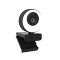 Black USB computer webcam with a magnetic privacy cover on a desk next to a laptop.