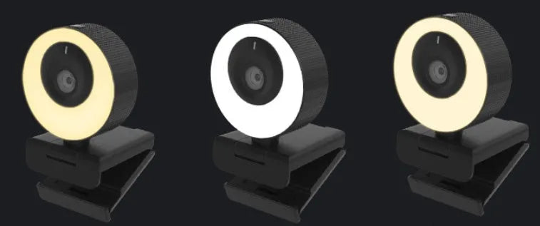 Black USB computer webcam with a magnetic privacy cover on a desk next to a laptop.