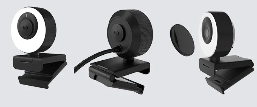 Black USB computer webcam with a magnetic privacy cover on a desk next to a laptop.