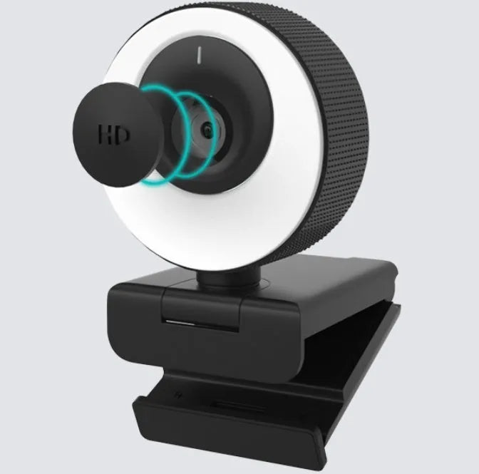 Black USB computer webcam with a magnetic privacy cover on a desk next to a laptop.