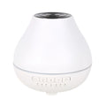 Round white Bluetooth humidifier and aroma diffuser with night light on a wooden surface.