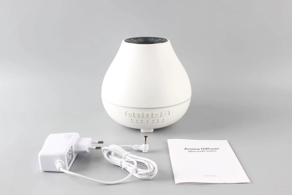 Round white Bluetooth humidifier and aroma diffuser with night light on a wooden surface.