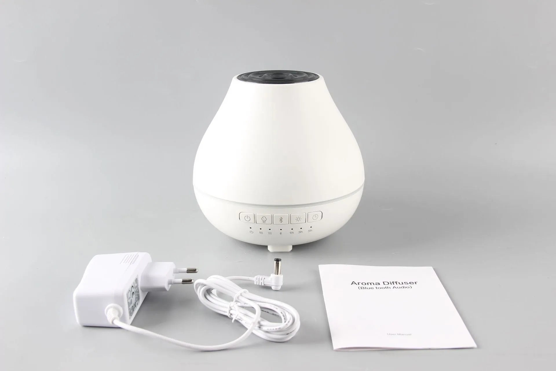 Round white Bluetooth humidifier and aroma diffuser with night light on a wooden surface.