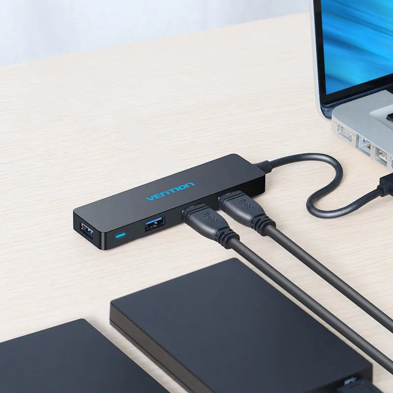 Black USB 3.0 four-port hub with a short cable and nickel-plated connectors on a desk.