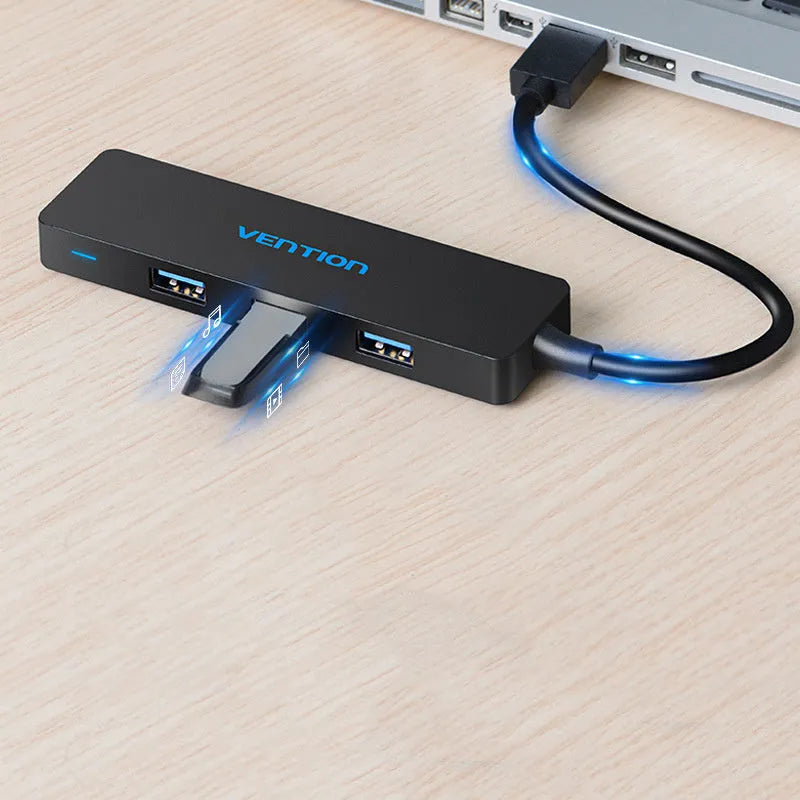 Black USB 3.0 four-port hub with a short cable and nickel-plated connectors on a desk.