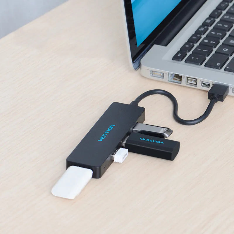 Black USB 3.0 four-port hub with a short cable and nickel-plated connectors on a desk.