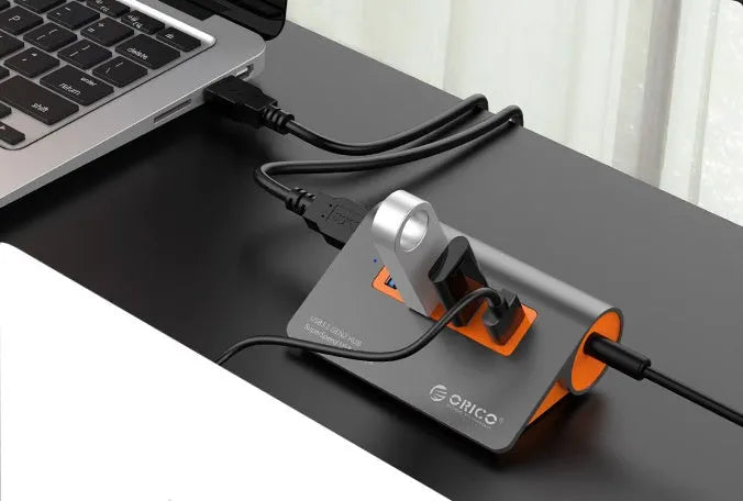 Dark grey and orange aluminium USB 3.1 laptop hub with four ports, separate cable, and power adapter