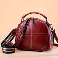 Round leather handbag with double soft handles and a zipper opening in a wine red colour.