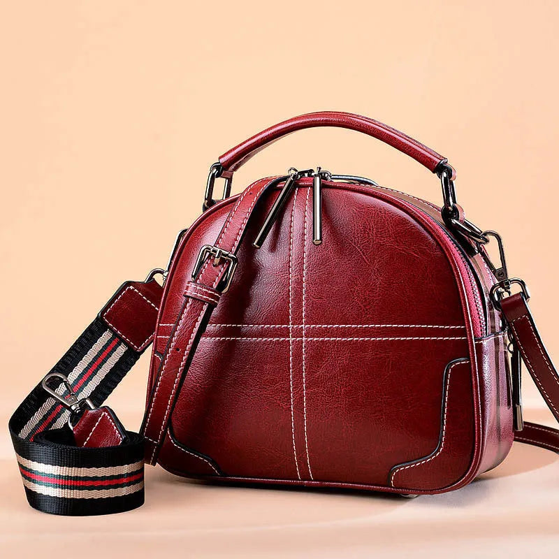 Round leather handbag with double soft handles and a zipper opening in a wine red colour.