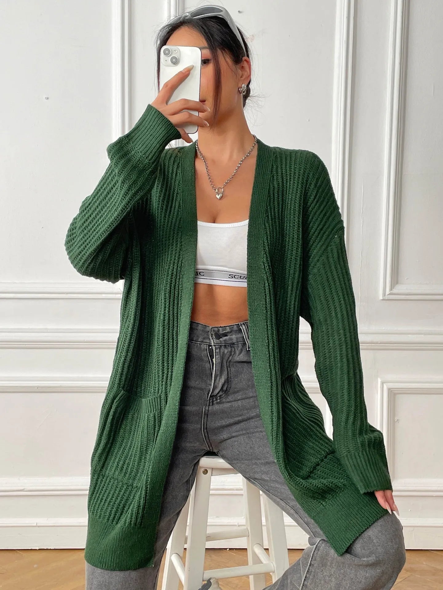 Women's dark green loose fit acrylic cardigan sweater with long sleeves on a hanger.