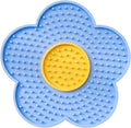 Flower-shaped silicone pet licking mat in blue with suction cups on the back, shown on a tiled surface.