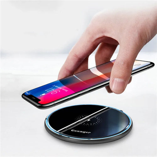 Black Qi fast wireless charging pad on a desk next to a smartphone, showing a blue LED charging indicator light.