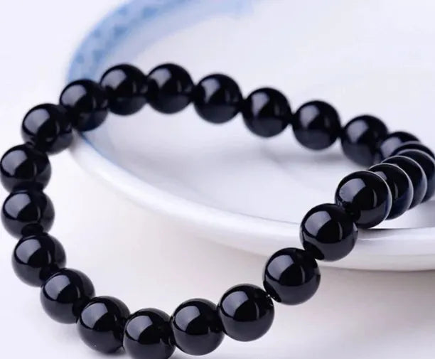 Close-up of a women's black onyx bracelet with 8mm geometric agate beads on a black elastic cord.