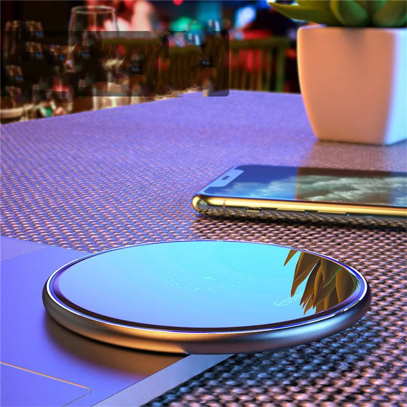Black Qi fast wireless charging pad on a desk next to a smartphone, showing a blue LED charging indicator light.