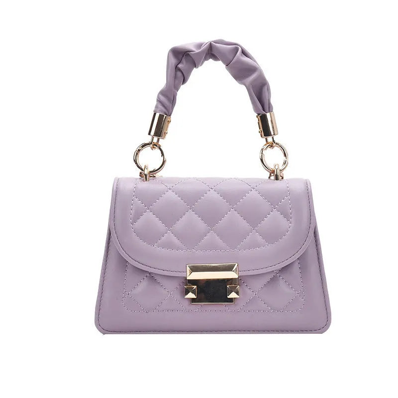 Purple soft PU leather small square shoulder bag with a long strap on a table.